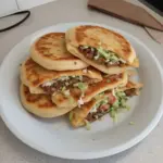 Homemade Mexican Gorditas filled with cheese and salsa on a wooden table.